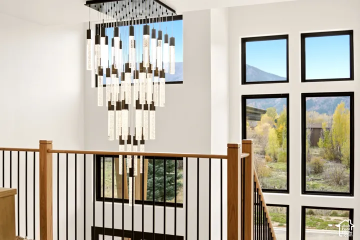 Multi-tiered statement chandelier, floor-to-ceiling windows, and a oak-topped railing with vertical metal balusters