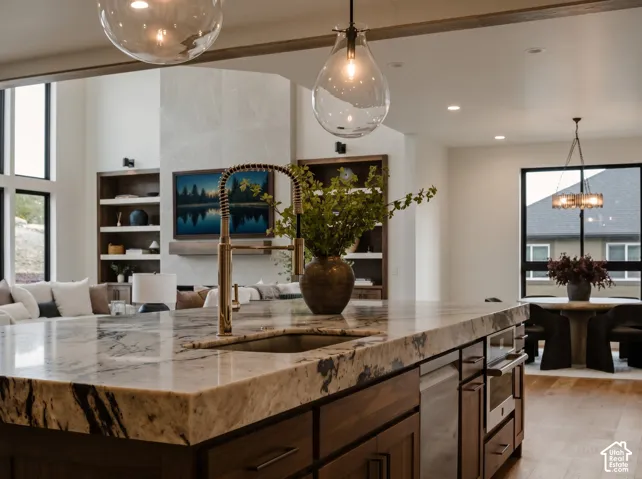 Dramatic 4" Tempest Crystal Quartzite 12'x5' Kitchen island featuring, under mount ash grey Kohler sink, and French gold faucet, paired with walnut cabinetry, built-in shelving, and statement pendant lighting