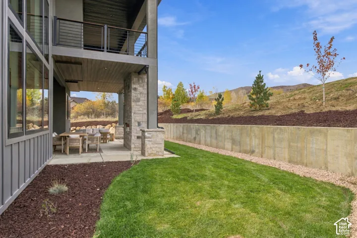Covered patio featuring a floor-to-ceiling limestone fireplace, metal railing system, concrete retaining wall, and landscape beds