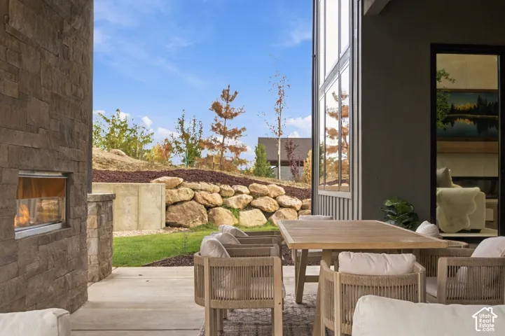Covered outdoor living space featuring dry-stacked natural limestone fireplace, concrete patio, built-in natural rock retaining wall, and landscaped grounds