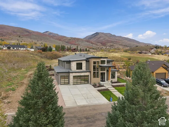 Contemporary exterior featuring dry-stacked natural limestone facade, multi-story glass paneling, double full view glass-paneled garage doors, set against a prominent mountain backdrop