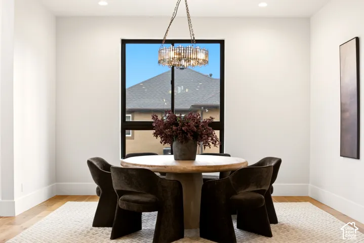 Dining space featuring engineered hardwood flooring, a large black-trimmed window, and a Arhaus chandelier with metallic accents