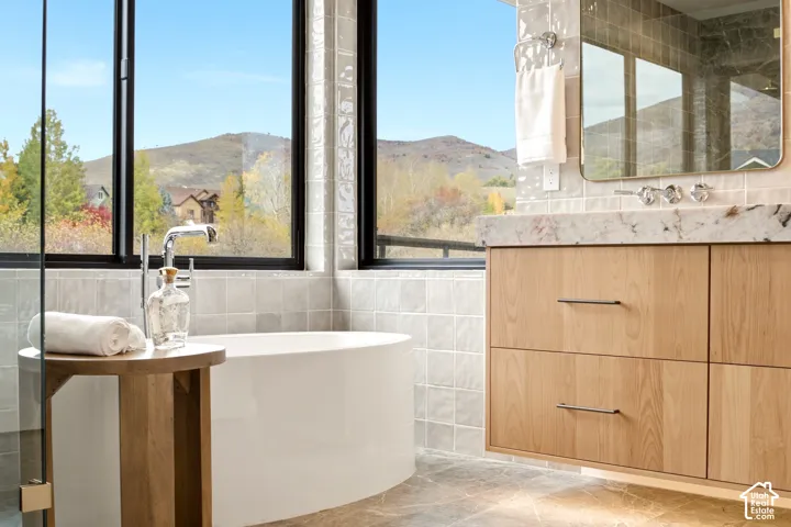 Primary Bathroom Freestanding acrylic white soaking tub, floating vanity with Tempest Crystal Quartzite countertop, large black windows, glass box shower, and tile bar tile wall surround