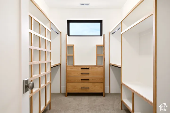 "Her" Walk-in Primary closet featuring custom oak-trim shelving, built-in dresser with Ash grey hardware, clerestory window, and carpeted flooring. (Not shown is the separate "His" Walk in closet)