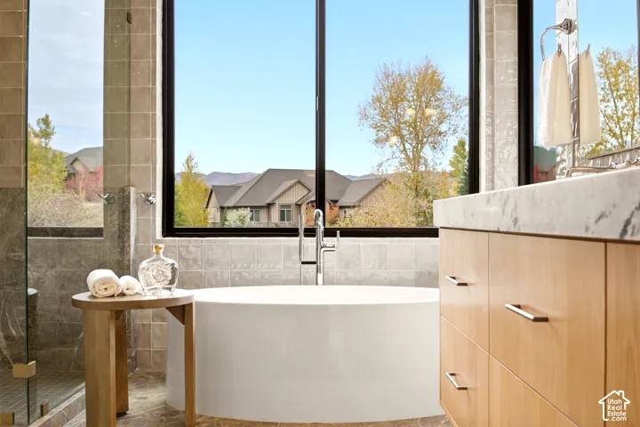 Primary Bathroom Freestanding acrylic white soaking tub, floating vanity with Tempest Crystal Quartzite countertop, large black windows, glass box shower, and tile bar tile wall surround