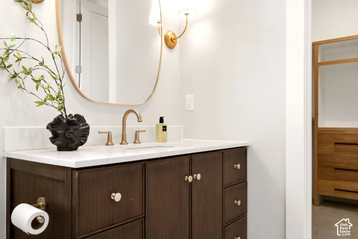Main Level Guest En-Suite Bathroom stained wood vanity with fluted cabinetry, brass-finish fixtures, oval mirror, wall-mounted sconces, and custom built-in walk in closet
