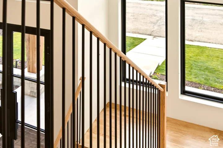 Staircase featuring an oak handrail, vertical matte black metal balusters, oak flooring, and black floor-to-ceiling windows