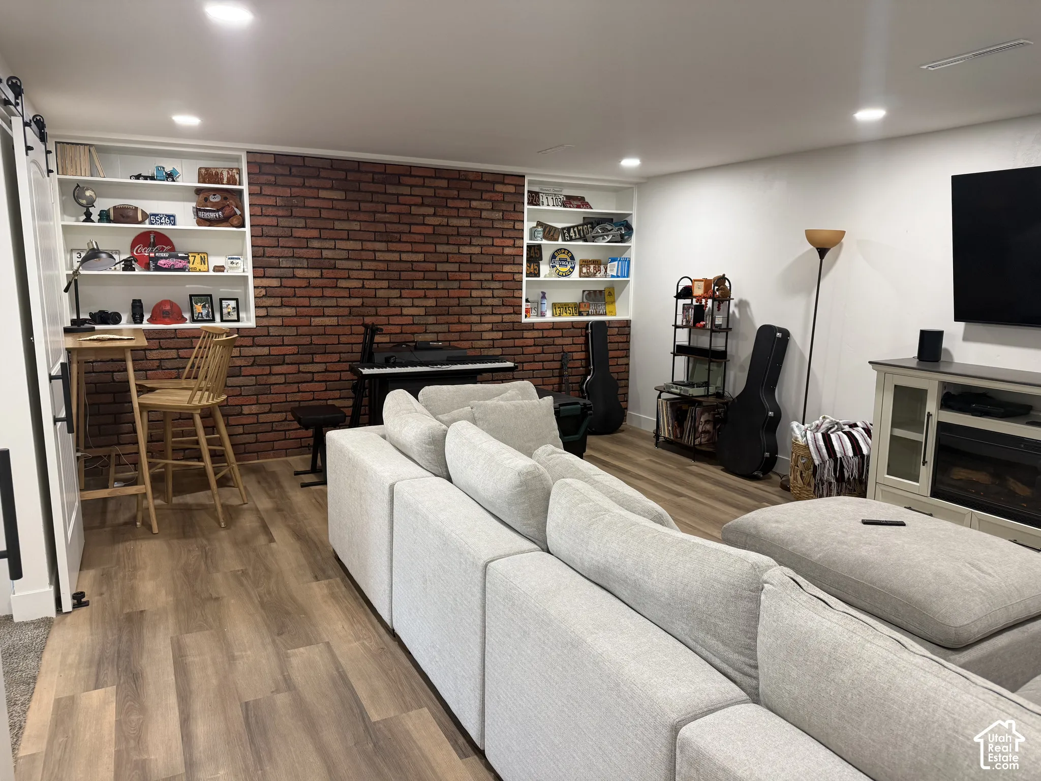 Exposed brick wall accenting built-in shelving, wood-finish flooring, and recessed ceiling lighting