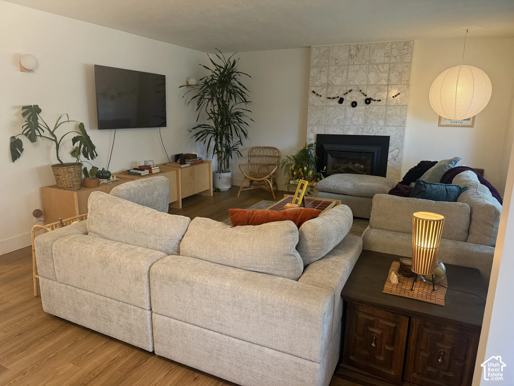 Living area featuring wood-finish flooring, a full-height tiled fireplace surround, an integrated fireplace insert, dual wall-mounted globe light fixtures, and a spherical paper pendant light