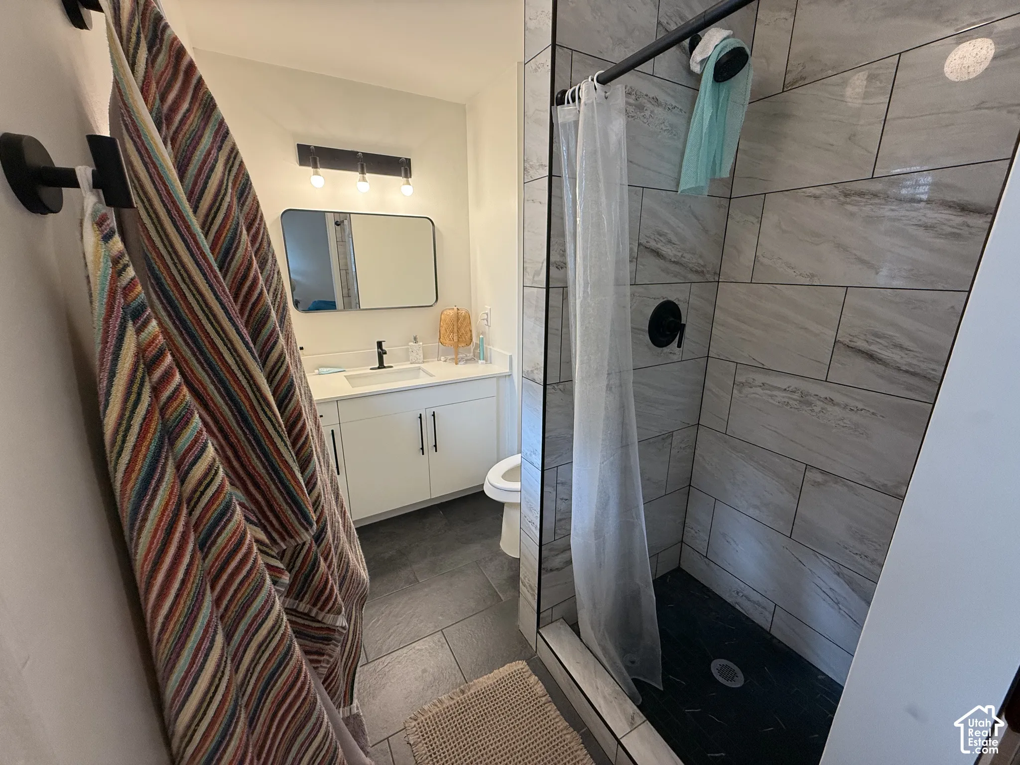 Bathroom featuring a white vanity with a solid-surface countertop, rectangular sink, matte black hardware, and a walk-in shower with large-format horizontal wall tile