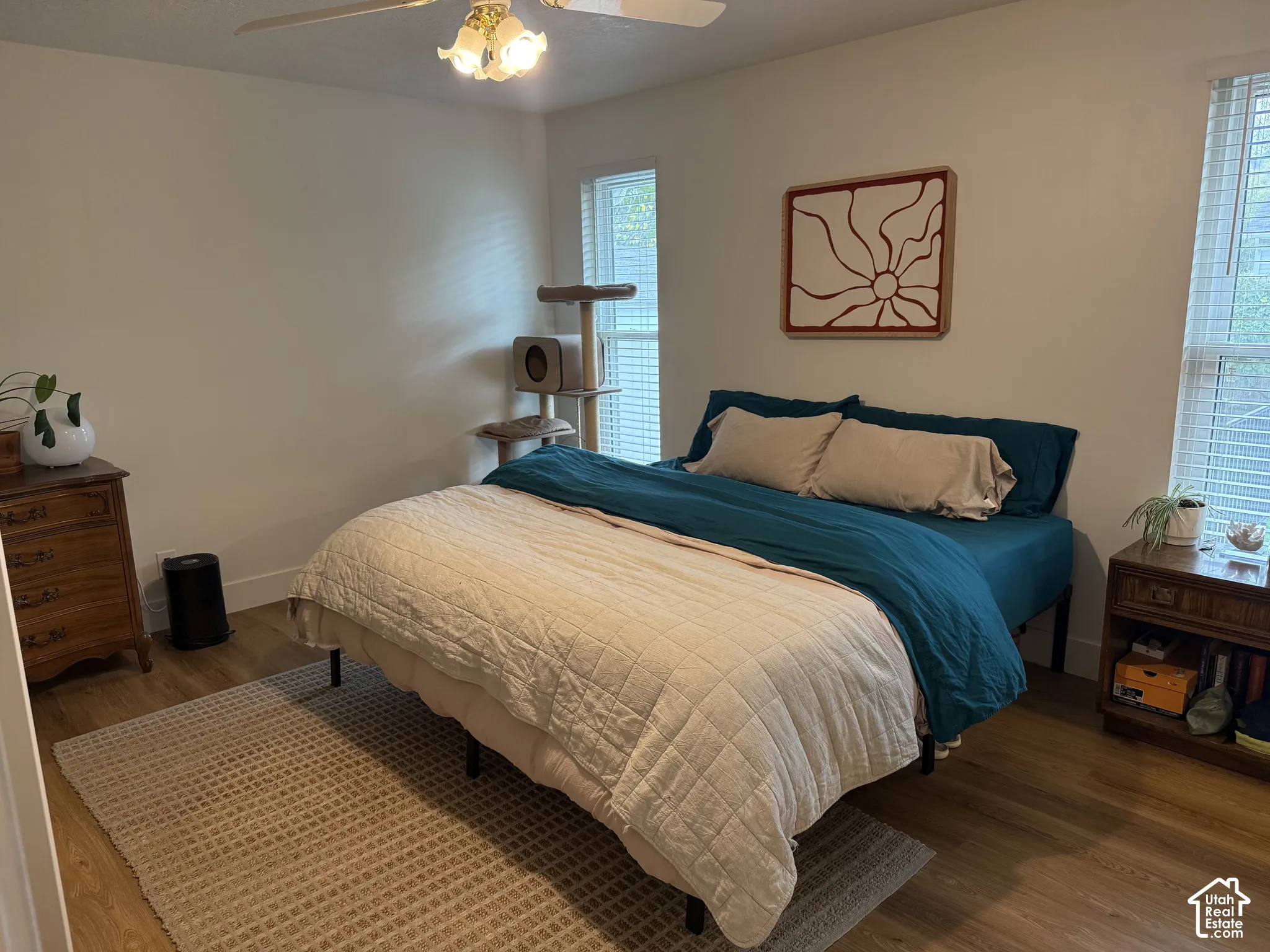 Neutral-toned room featuring wood-finish flooring, two windows with horizontal blinds, and a central ceiling fan with integrated lighting