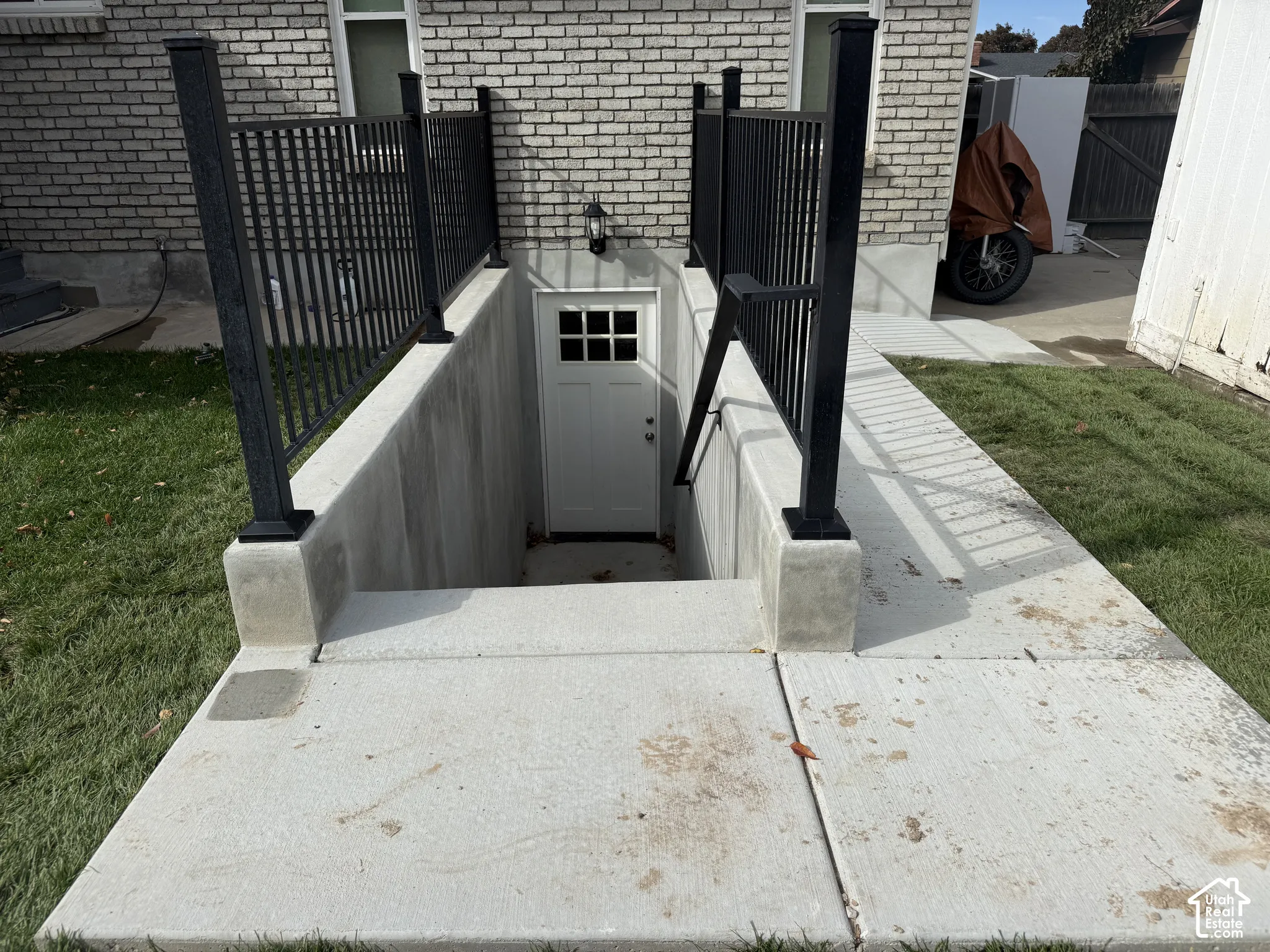 Exterior entrance featuring a concrete stairwell, black metal railings, and a multi-pane glass door set against a light-colored brick facade