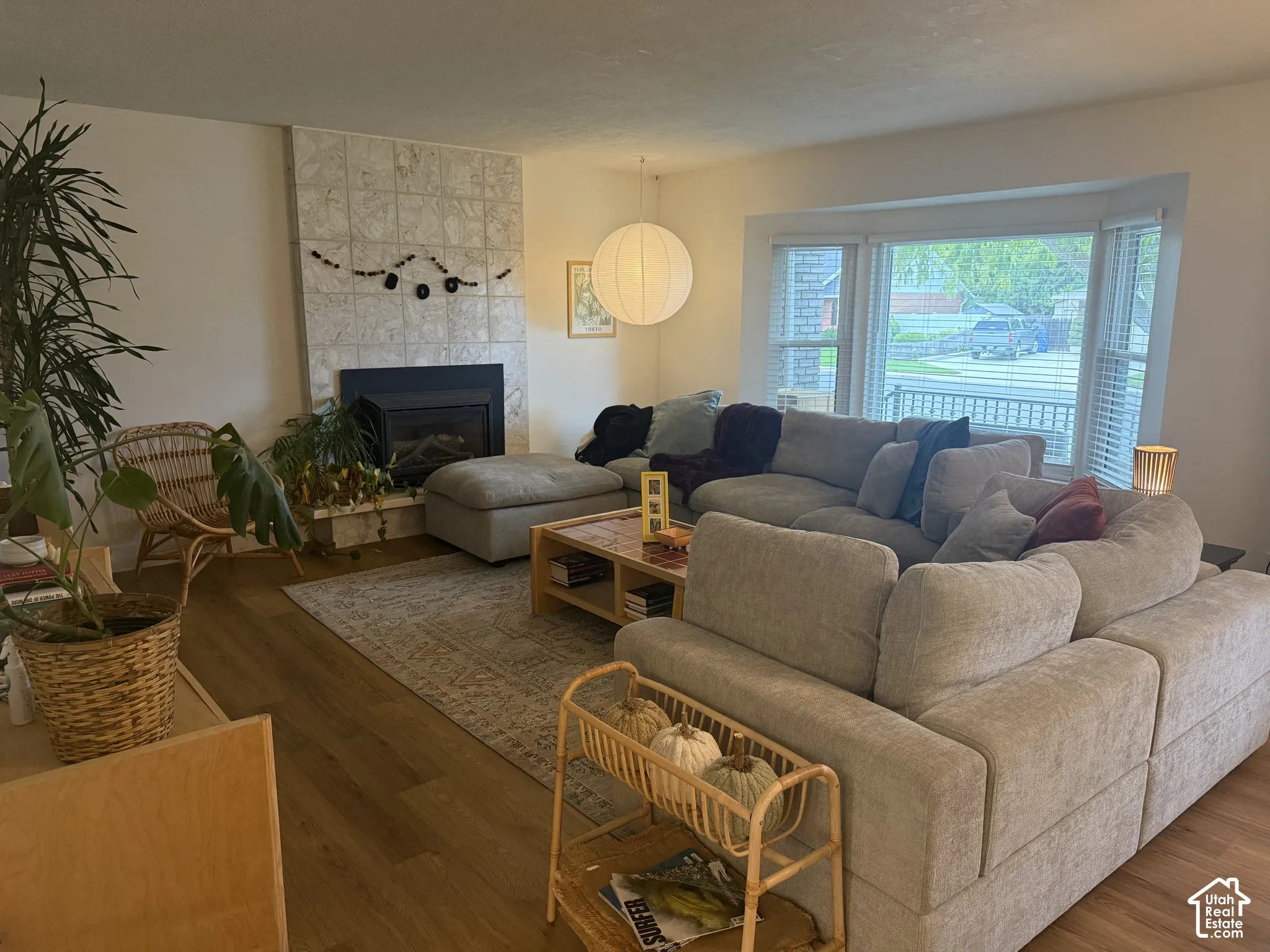 Living area featuring wood-finish flooring, a tile-surround fireplace, a bay window, and a spherical pendant light