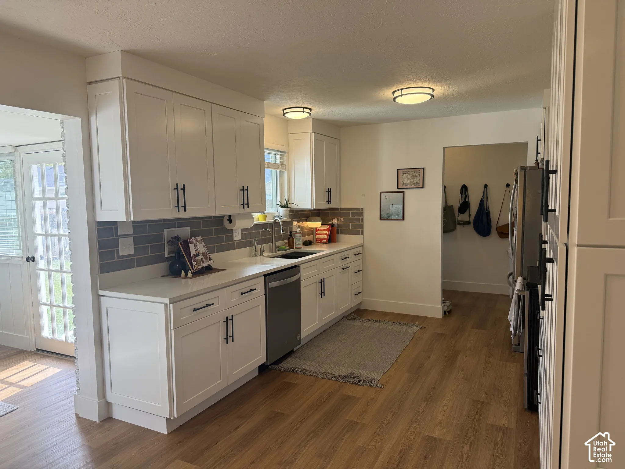 Kitchen featuring white shaker-style cabinetry, solid-surface countertops, gray subway tile backsplash, stainless steel appliances, and wood-finish flooring