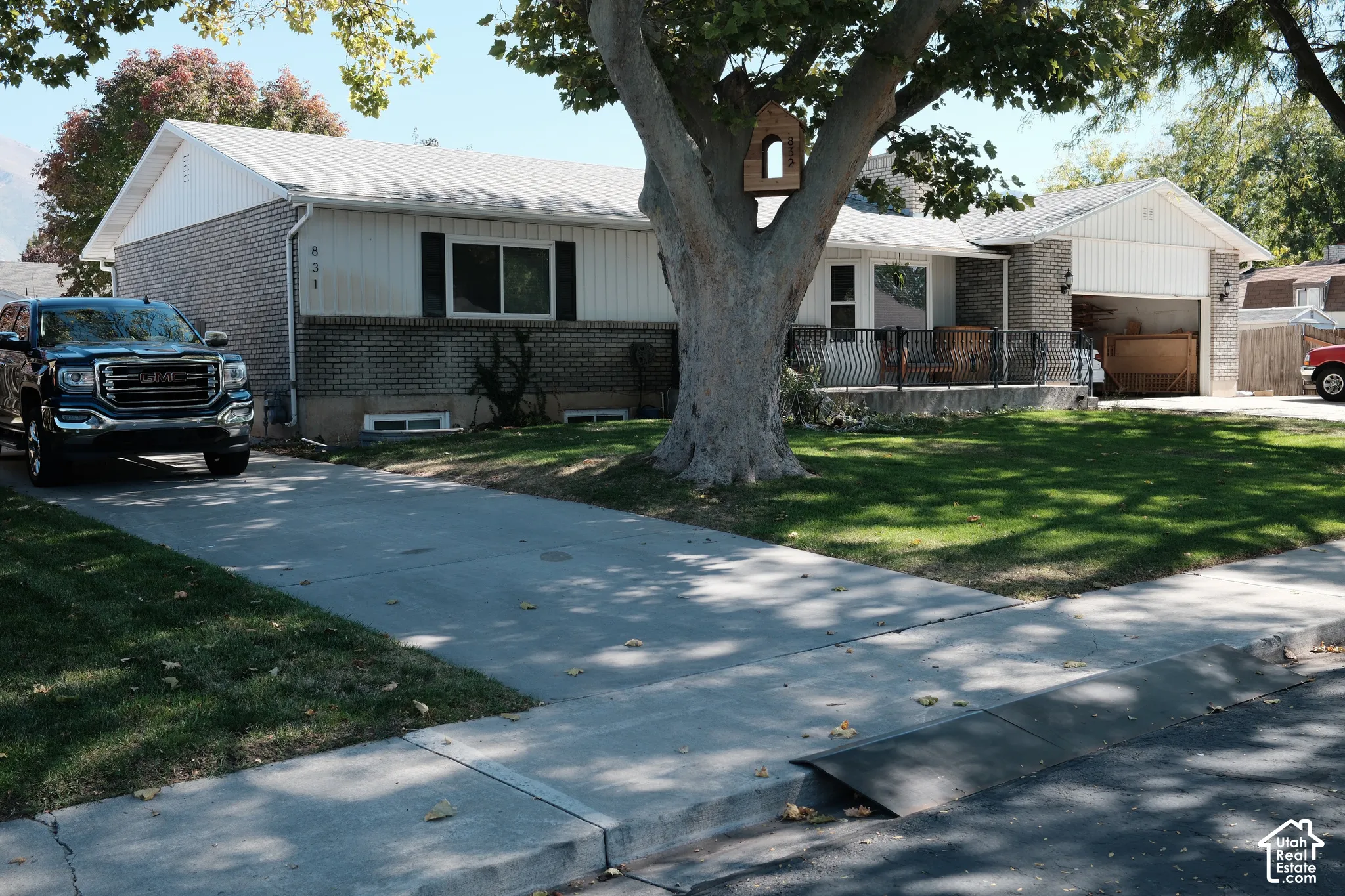 Single-story exterior featuring a brick and vertical siding facade, concrete driveway, attached garage, and a covered front porch with iron railings