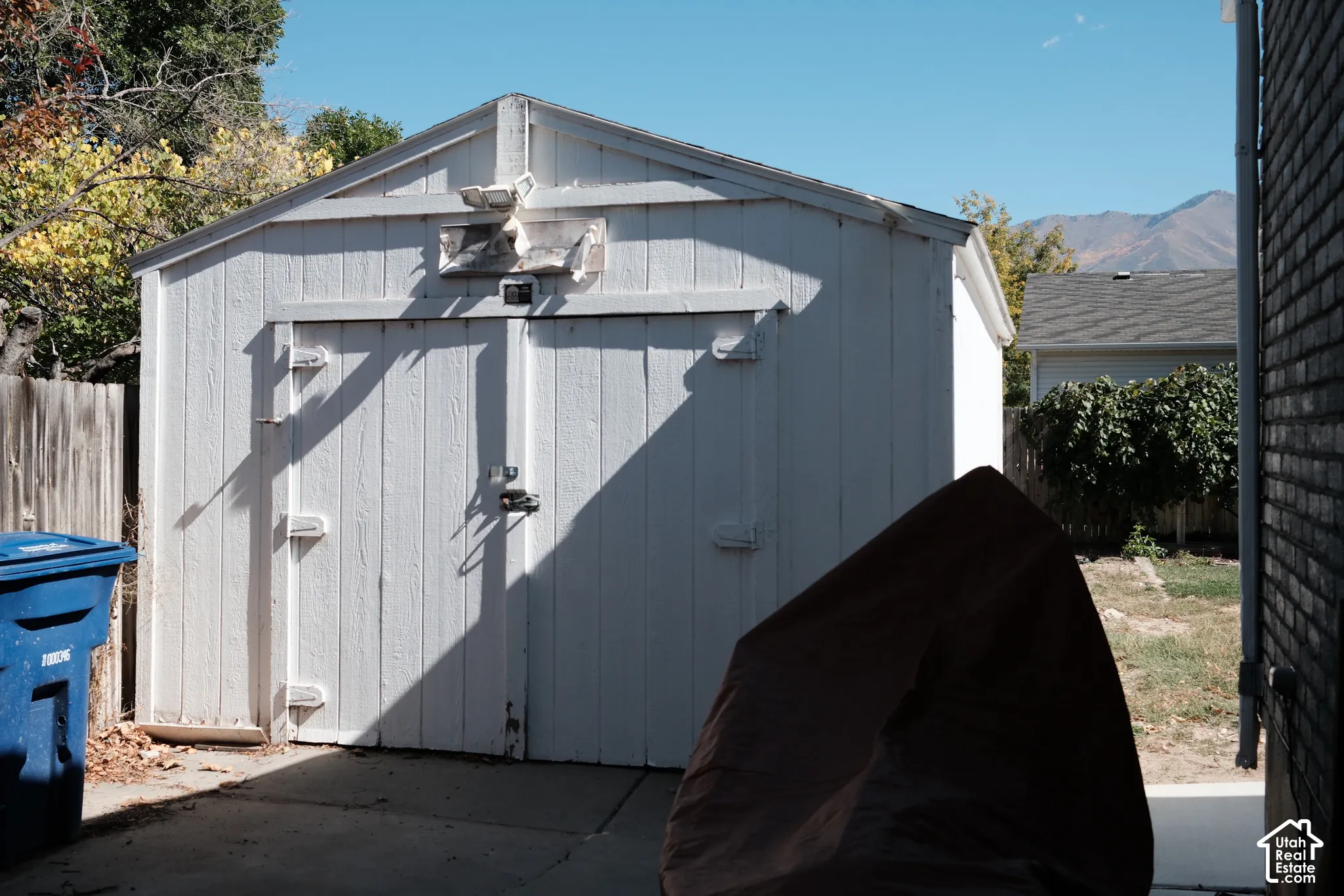 Detached white storage structure featuring double doors and exterior wall-mounted lighting