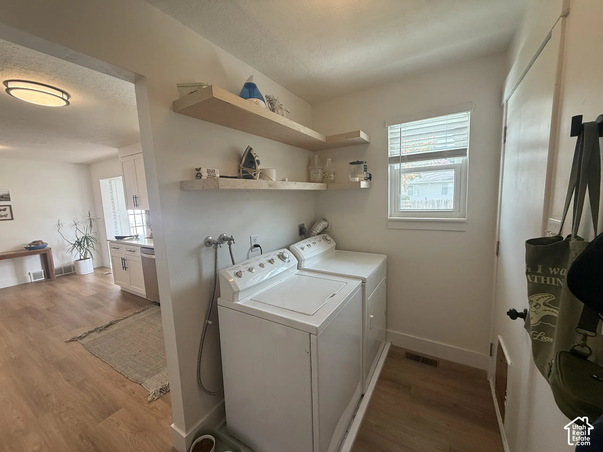 Laundry room featuring wood-finish flooring, floating natural wood shelving, and a single-hung window with built-in blinds