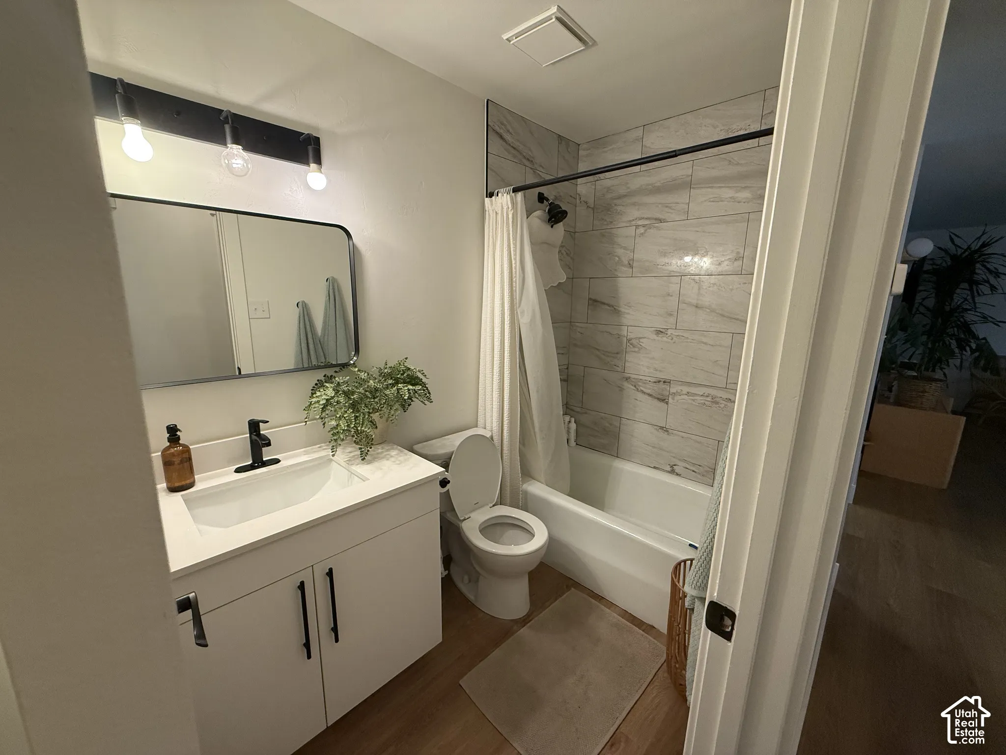 Modern vanity with a rectangular sink, matte black faucet, wall-mounted light fixture, and stone-finish tub surround with horizontal tiling