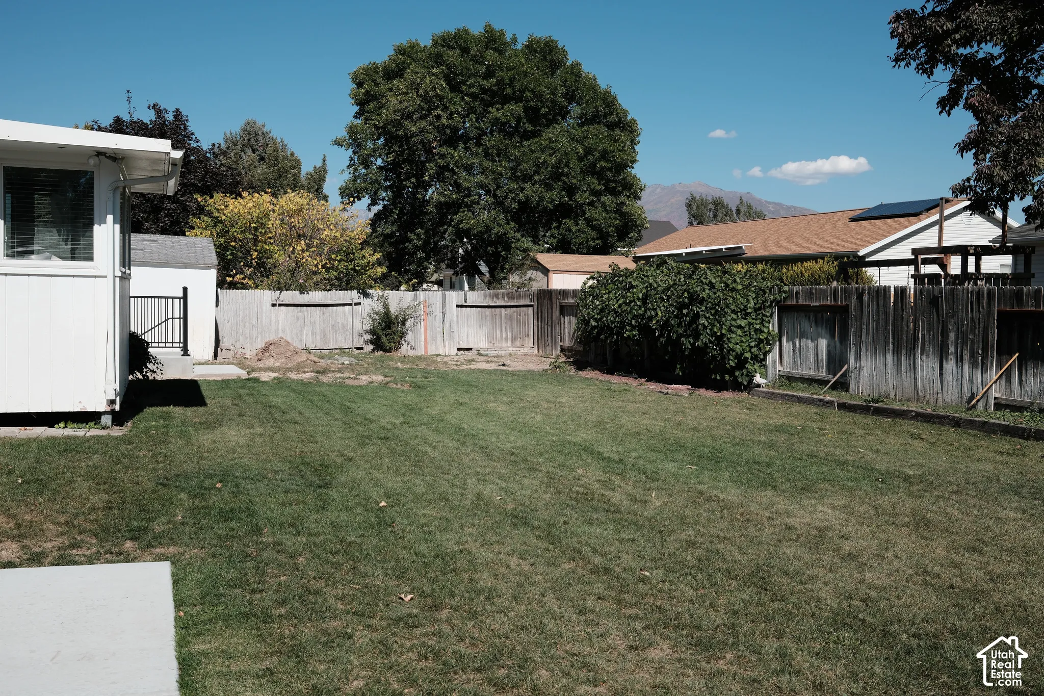 Fenced backyard featuring a grass lawn, concrete patio, and mountain backdrop