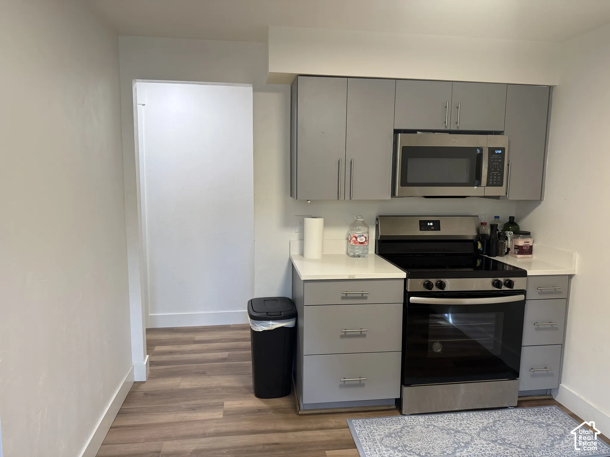 Kitchen featuring gray flat-panel cabinetry, stainless steel appliances, and white solid-surface countertops with wood-finish flooring