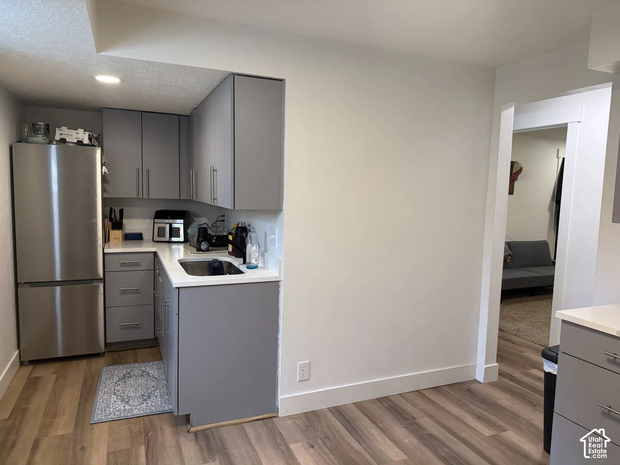 Kitchen area featuring flat-panel gray cabinetry, white countertops, stainless steel bottom-freezer refrigerator, and wood-finish flooring