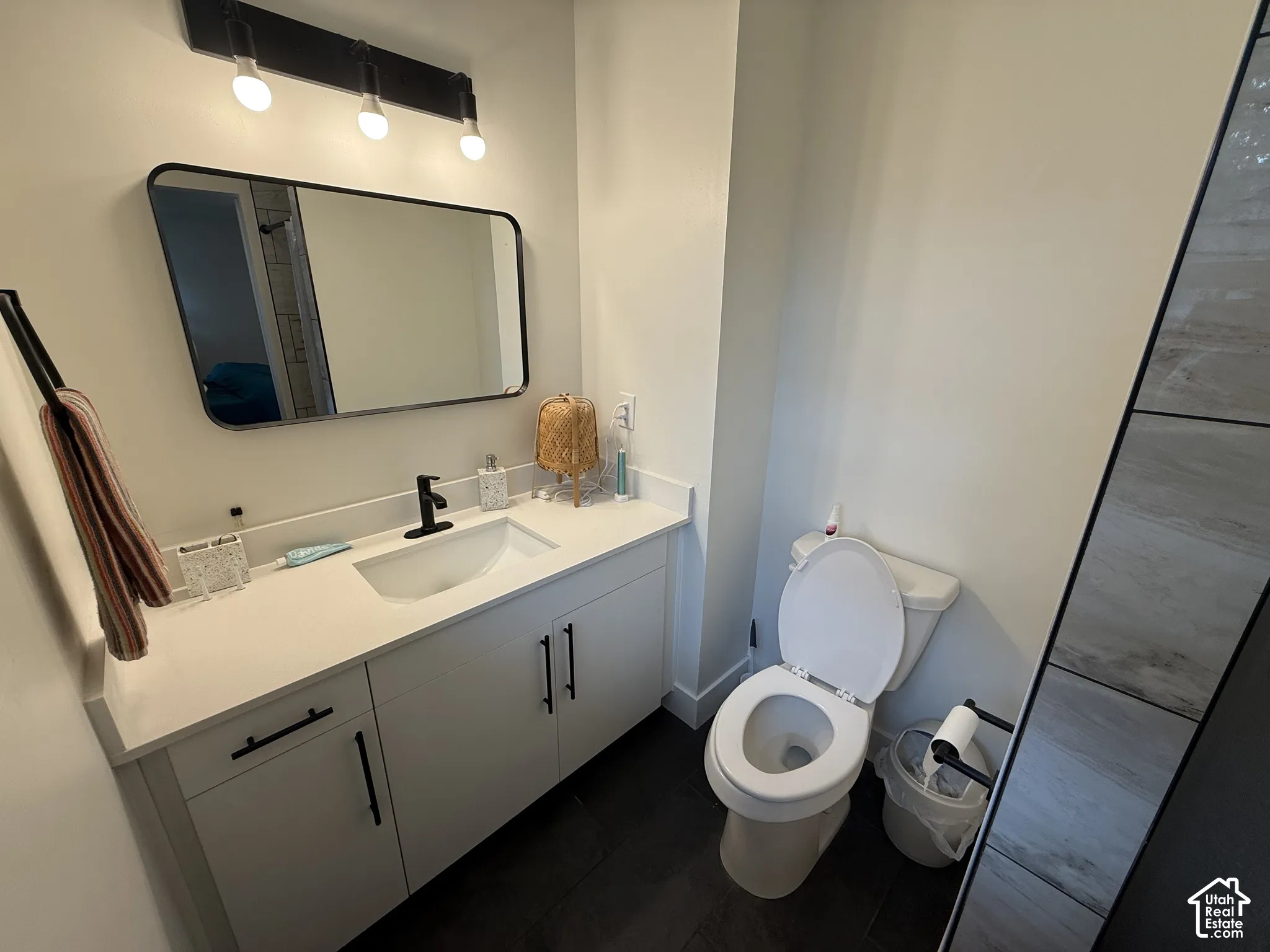 Bathroom featuring a vanity with quartz countertop, under-mount sink, matte black faucet, rectangular wall-mounted mirror, and dark tile flooring