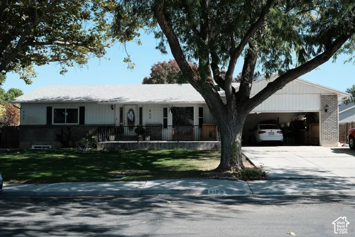 Single-story residence featuring light-toned vertical siding, a brick facade accent, a covered front porch with metal railing, and an attached two-car carport