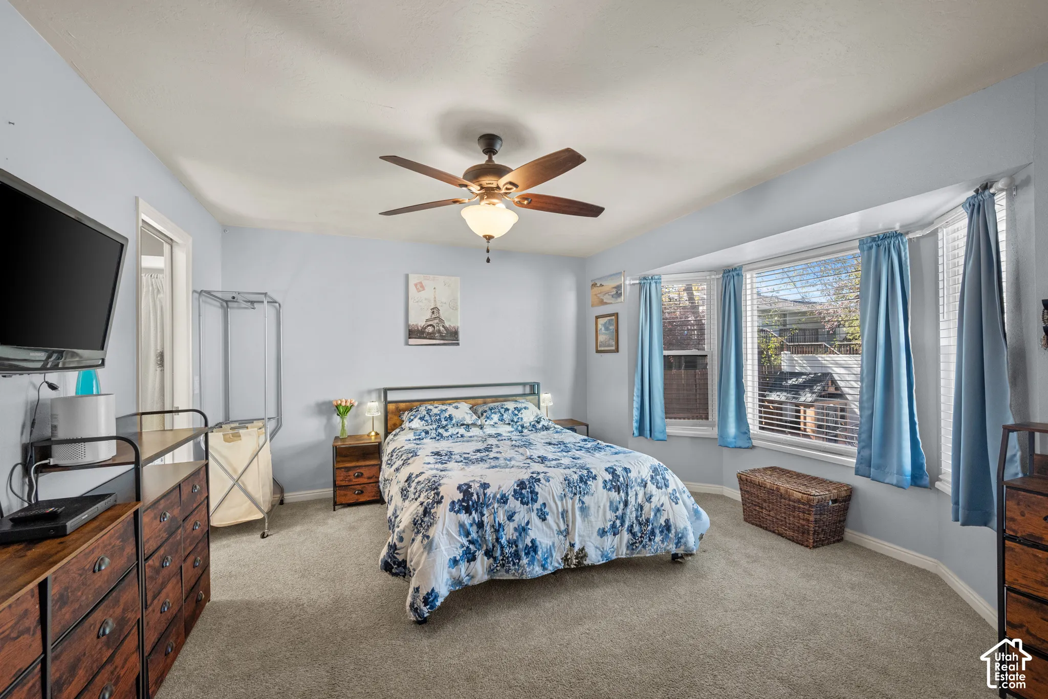 Bay window with multi-pane windows, neutral wall-to-wall carpeting, and a central ceiling fan with integrated lighting