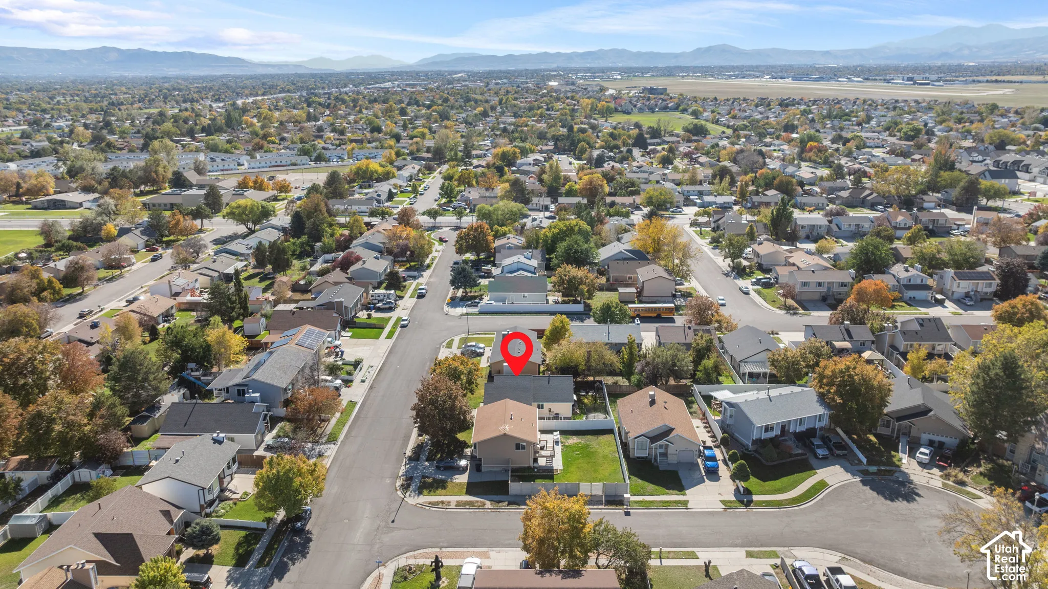Aerial perspective of a residential corner lot featuring a fenced backyard, mature trees, and a distant mountain backdrop