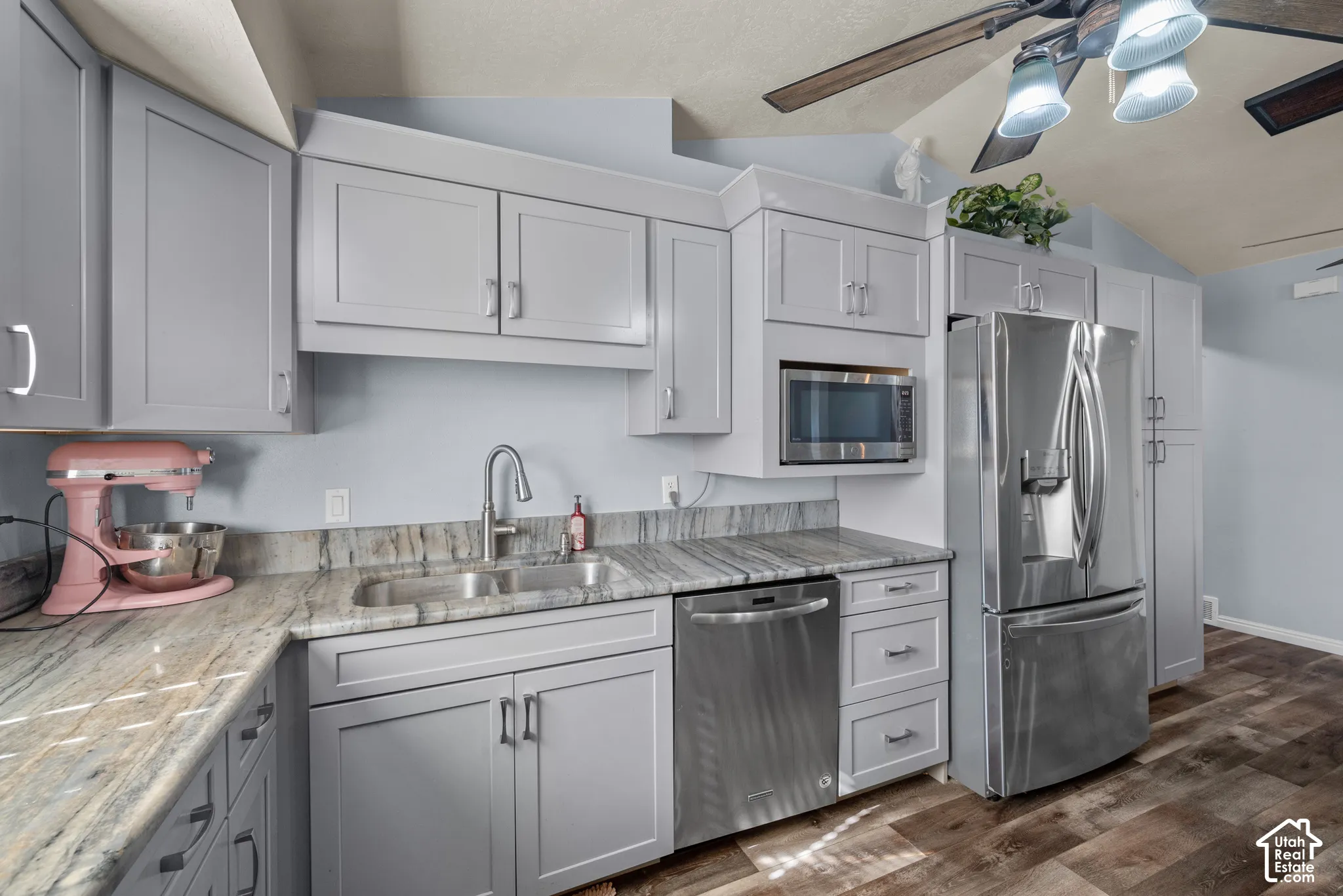 Kitchen featuring grey shaker-style cabinetry, patterned stone countertops, stainless steel appliances, a dual-basin undermount sink, and wood-finish flooring