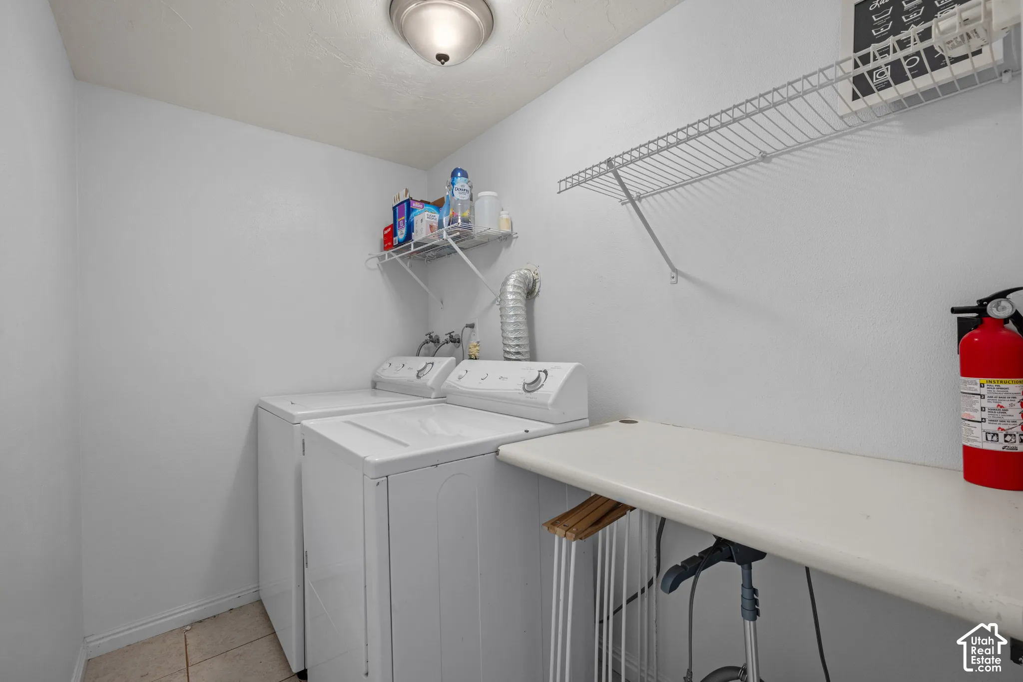 Laundry area featuring white appliance hookups, dual wall-mounted wire shelving units, and a built-in folding counter
