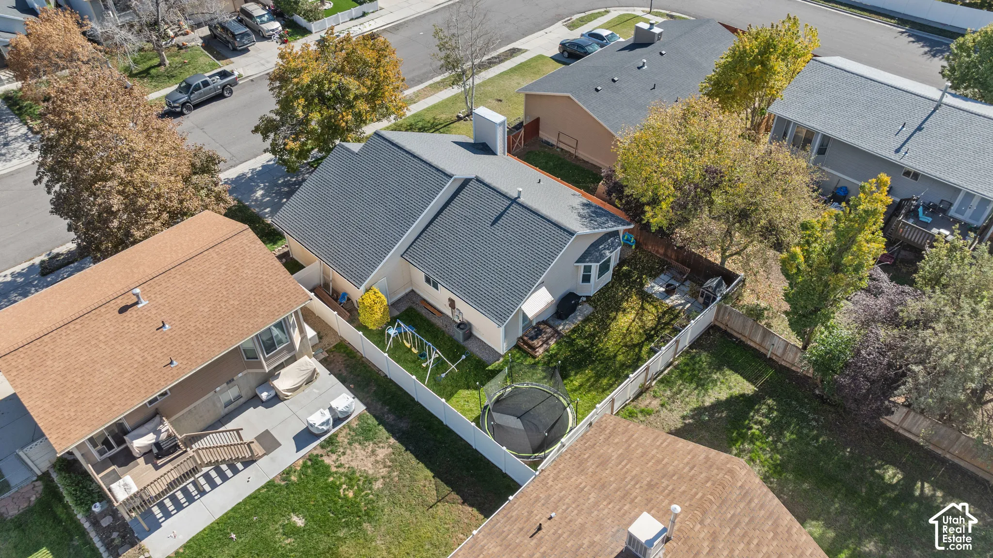 Aerial perspective of a detached residential property featuring a shingled roof, a chimney, an enclosed backyard with established trees, and perimeter fencing