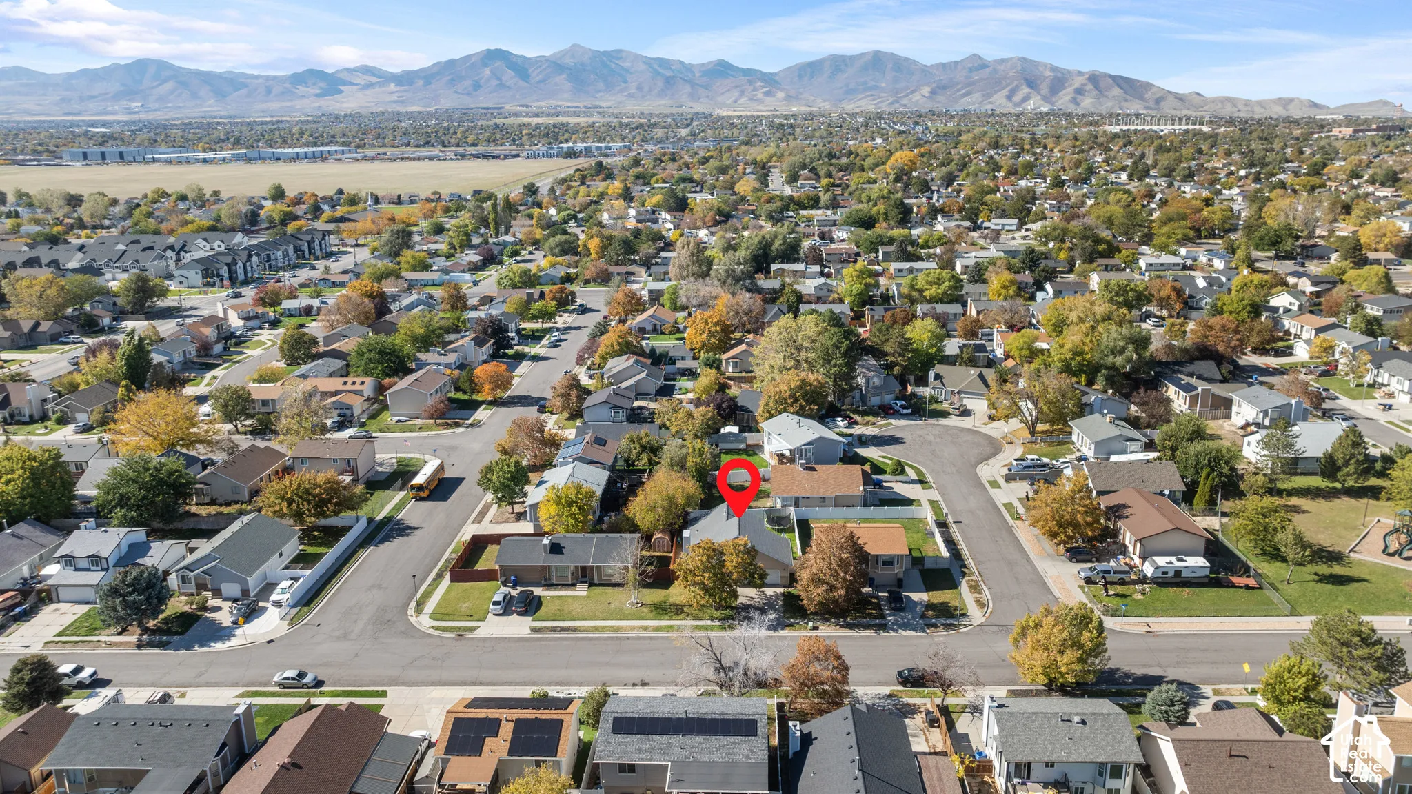 Aerial perspective of residential property featuring a composition shingle roof, mature deciduous trees, and a mountain range backdrop