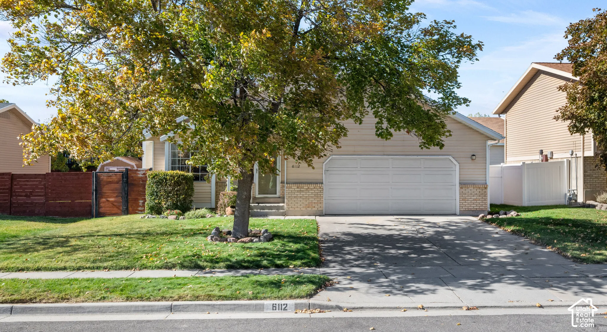 Single-story residence featuring a tan horizontal-siding and brick exterior, a two-car attached garage, a concrete driveway, and mature landscaping