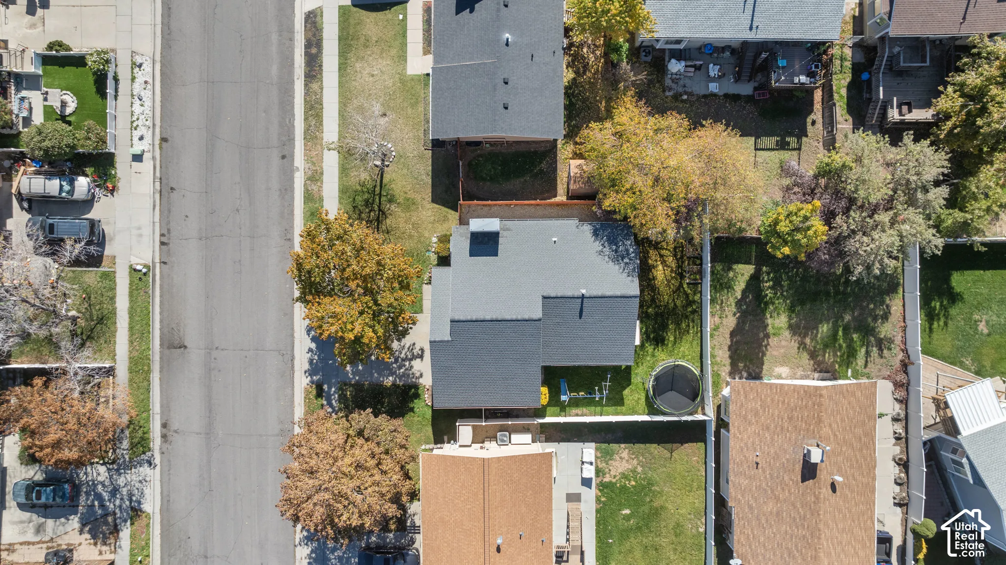 Aerial perspective of residential lot featuring a multi-pitched shingle roof, mature landscaping, and a fenced rear yard
