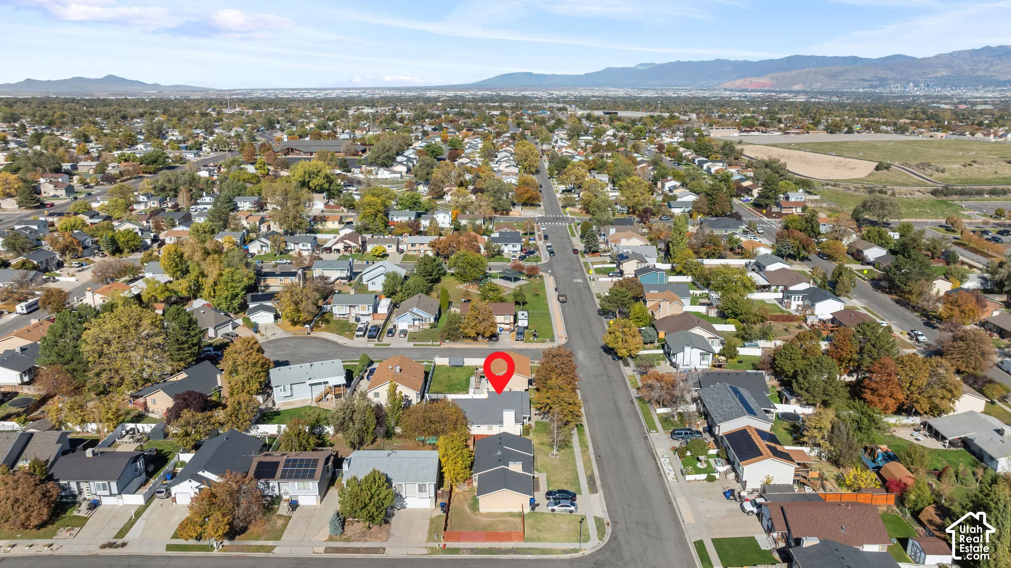 Aerial perspective of a residential property featuring an asphalt-shingle roof, a dedicated driveway, and a fenced backyard, set against a backdrop of mountain ranges