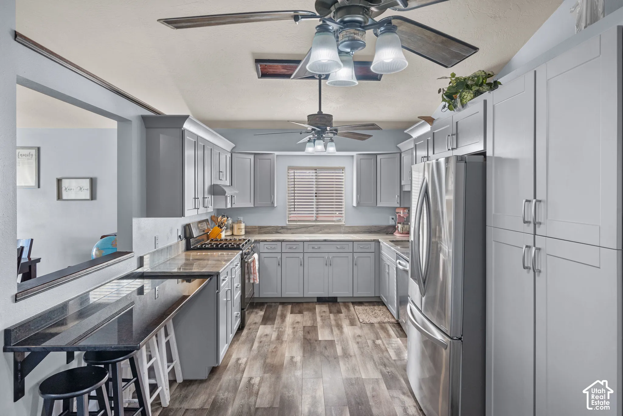 Kitchen featuring grey shaker-style cabinetry, wood-finish flooring, a built-in breakfast bar, stainless steel refrigerator, and dual ceiling fans
