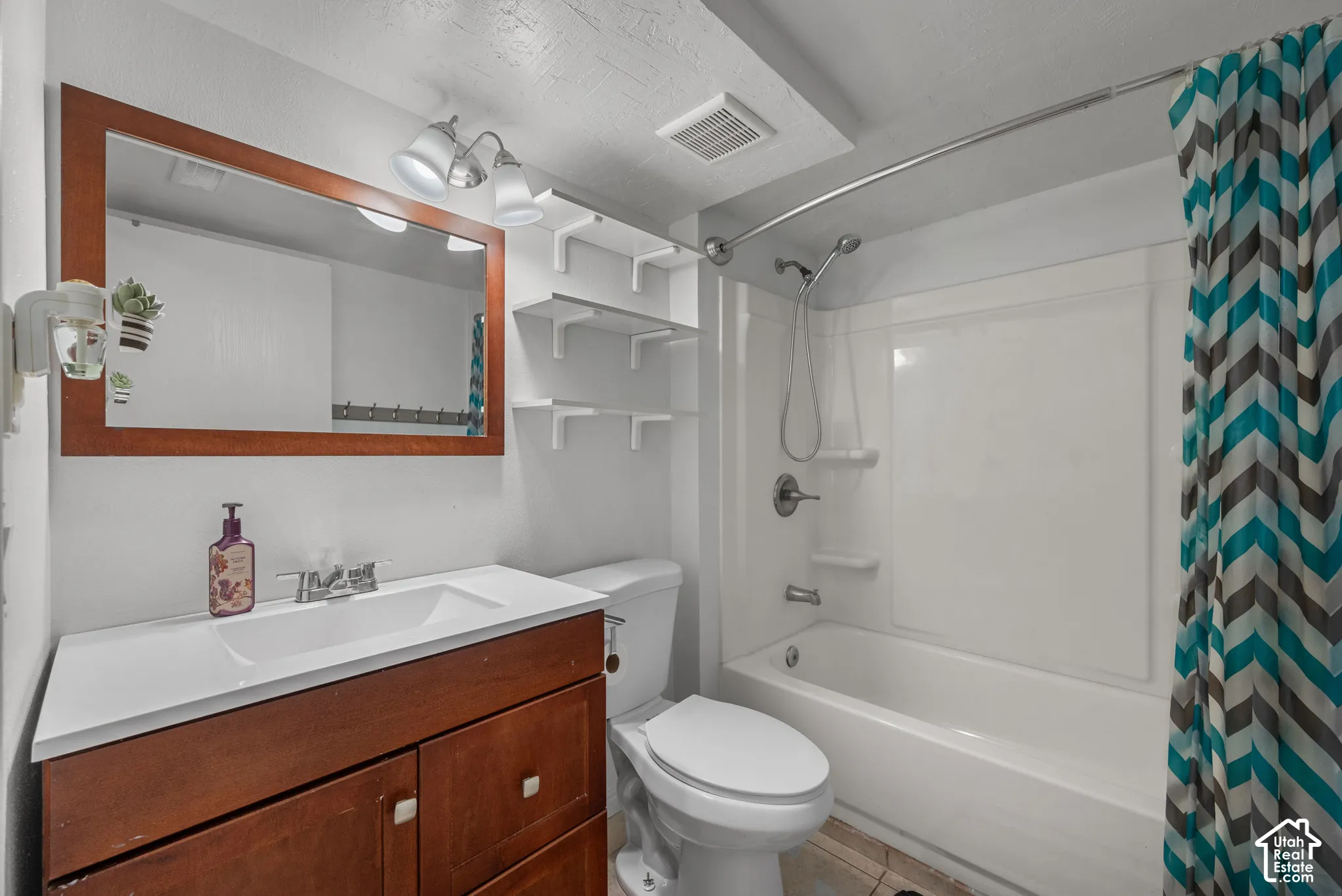 Wood-finish vanity with integrated sink, rectangular framed wall mirror, built-in wall shelving, and a combination tub and shower enclosure with a solid-surface surround