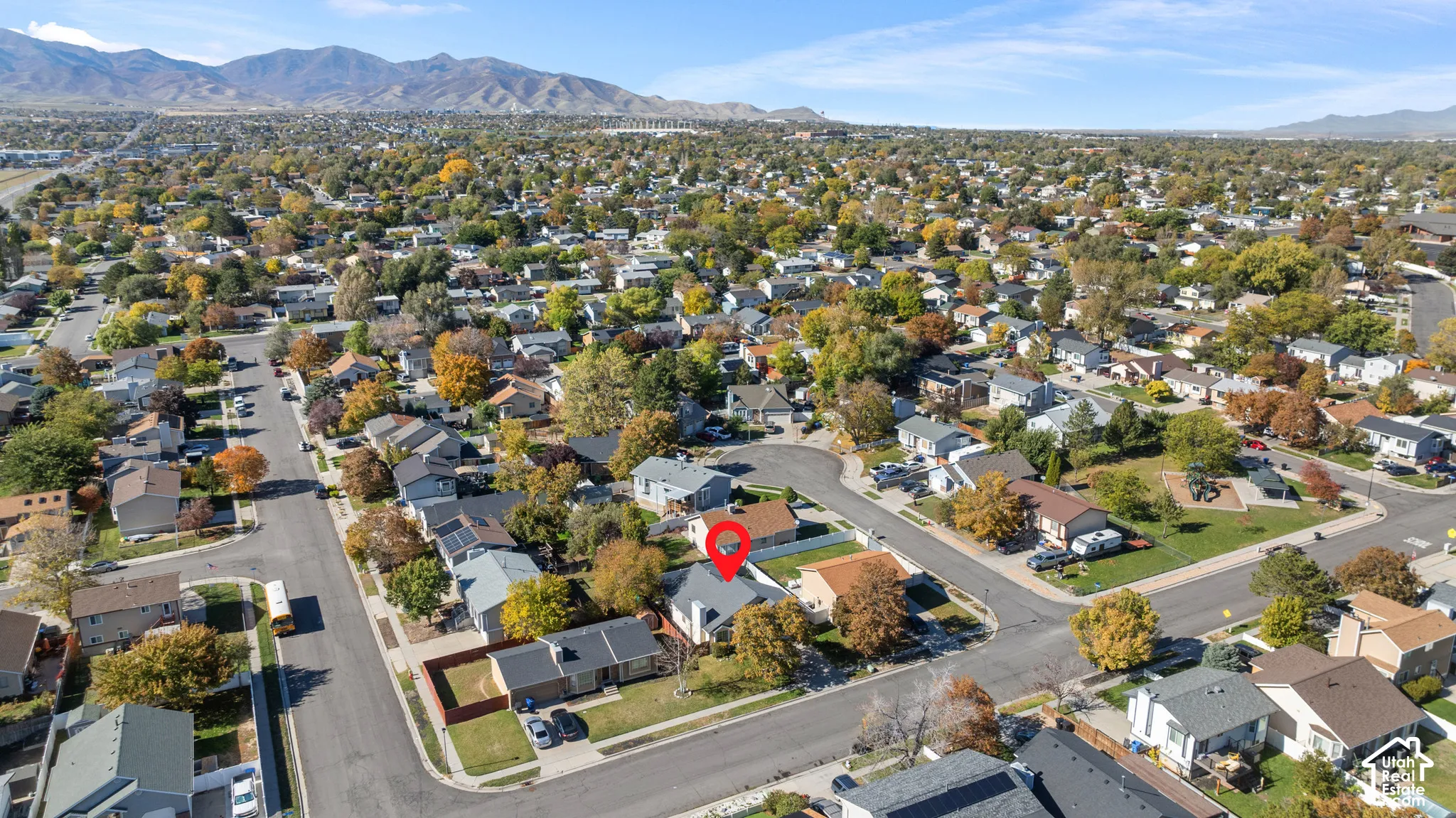 Aerial perspective of a single-family residence featuring a pitched roof, attached garage, private backyard with mature trees, and a mountain backdrop
