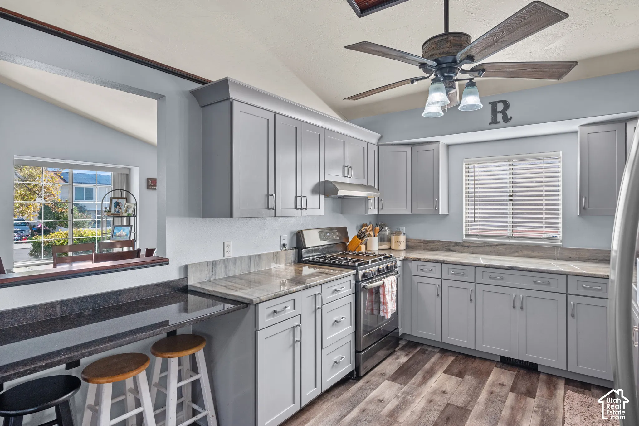 Kitchen featuring shaker-style grey cabinetry, stone-finish countertops, stainless steel gas range, integrated breakfast bar, and wood-finish flooring