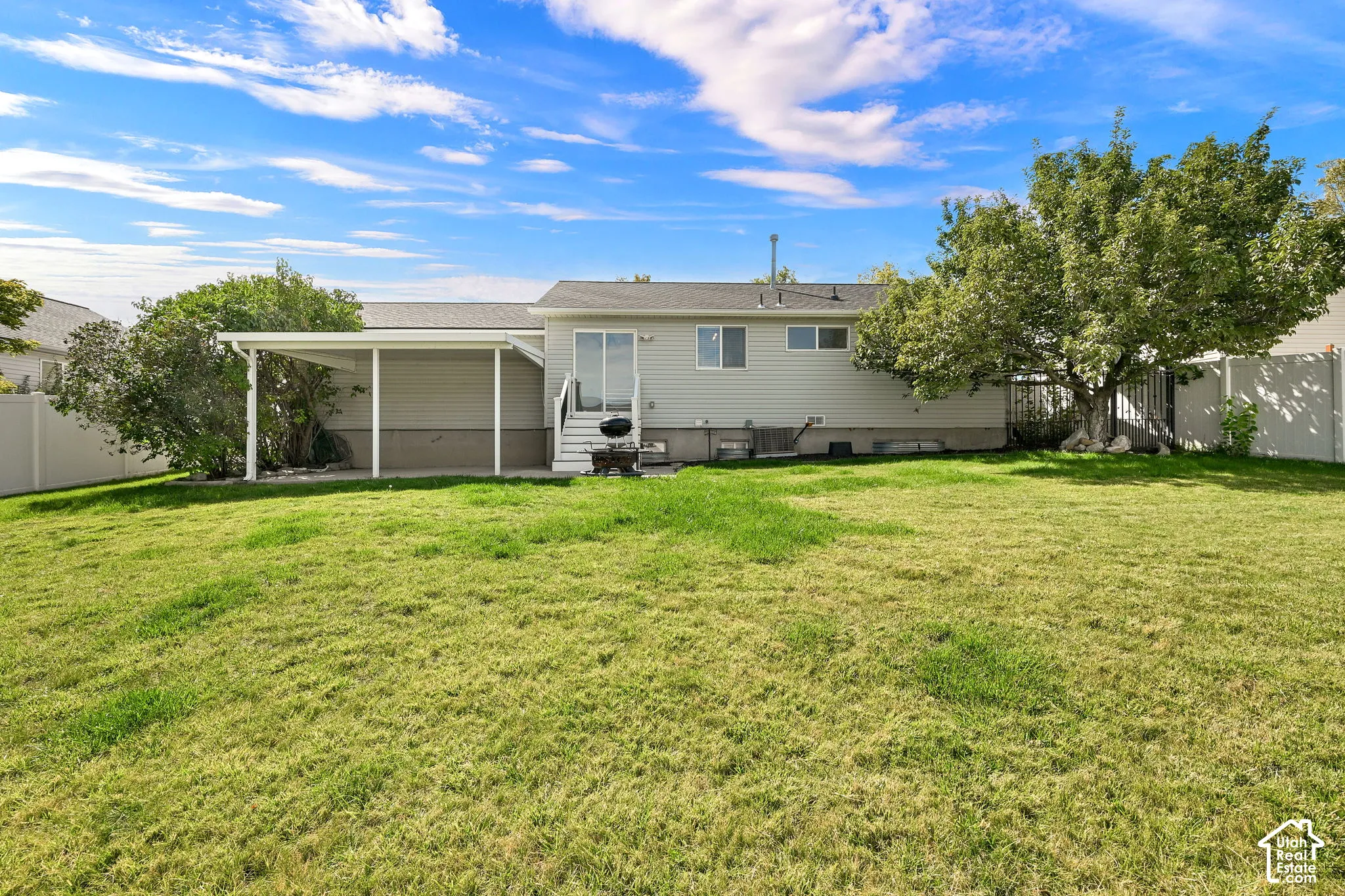Rear exterior featuring horizontal siding, a covered patio, and a grass-covered backyard enclosed by vinyl fencing