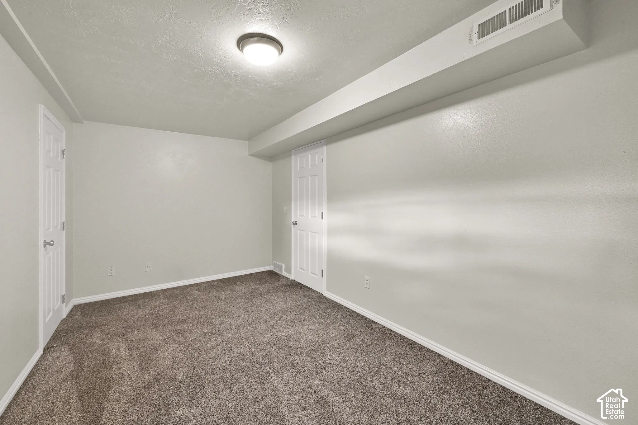 Neutral-toned room featuring neutral wall-to-wall carpeting, two interior doors, and a flush-mount ceiling light fixture