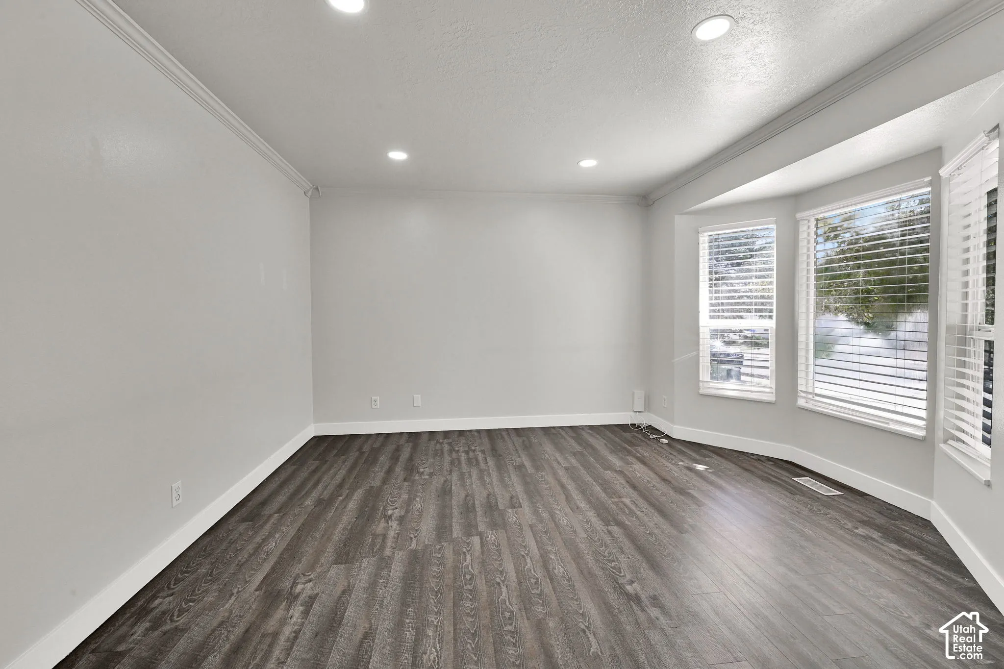 Room featuring wood-finish flooring, recessed lighting, crown molding, and a bay window equipped with horizontal blinds