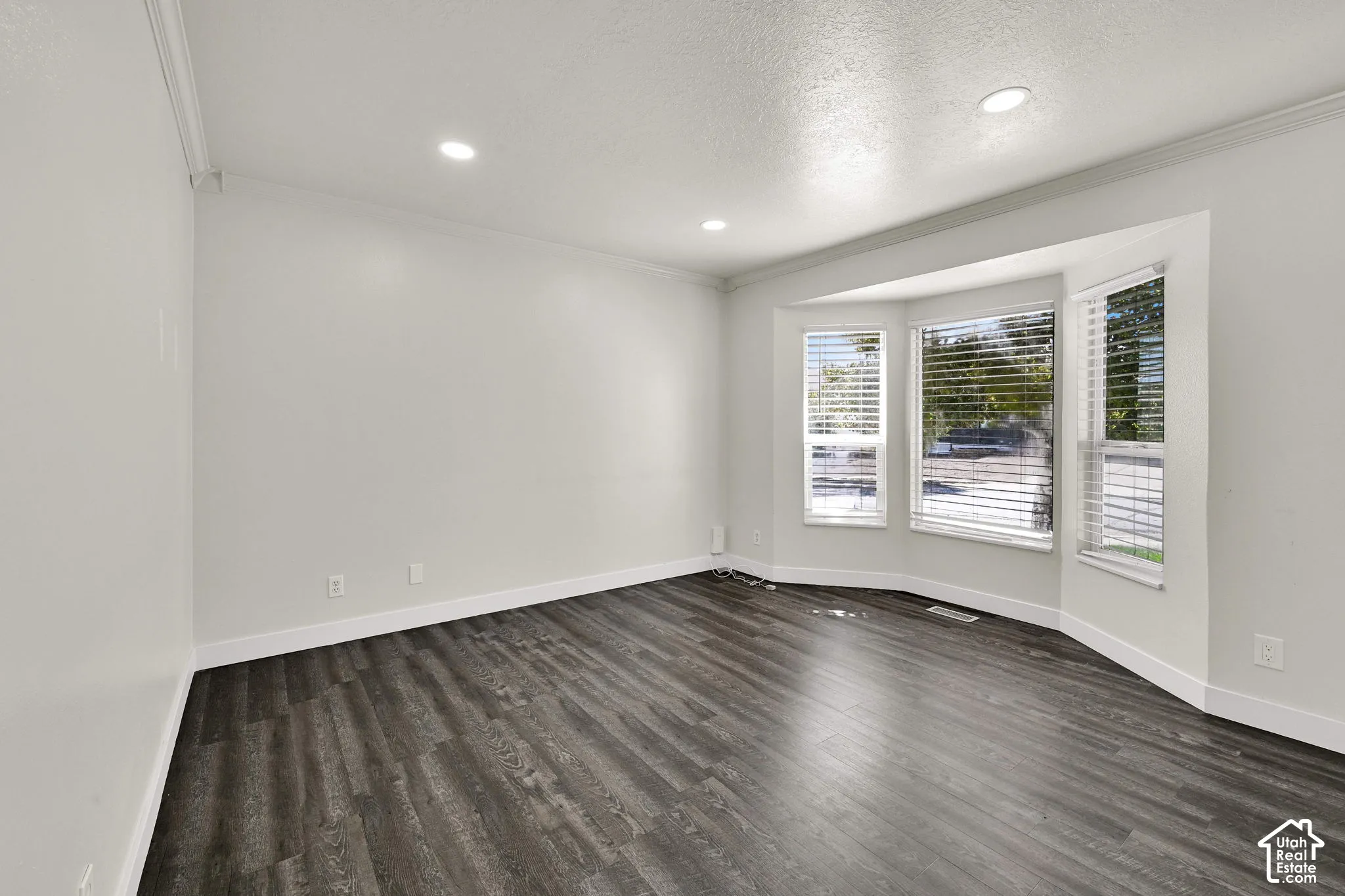 Interior room featuring wood-finish flooring, a three-panel bay window, crown molding, and recessed lighting