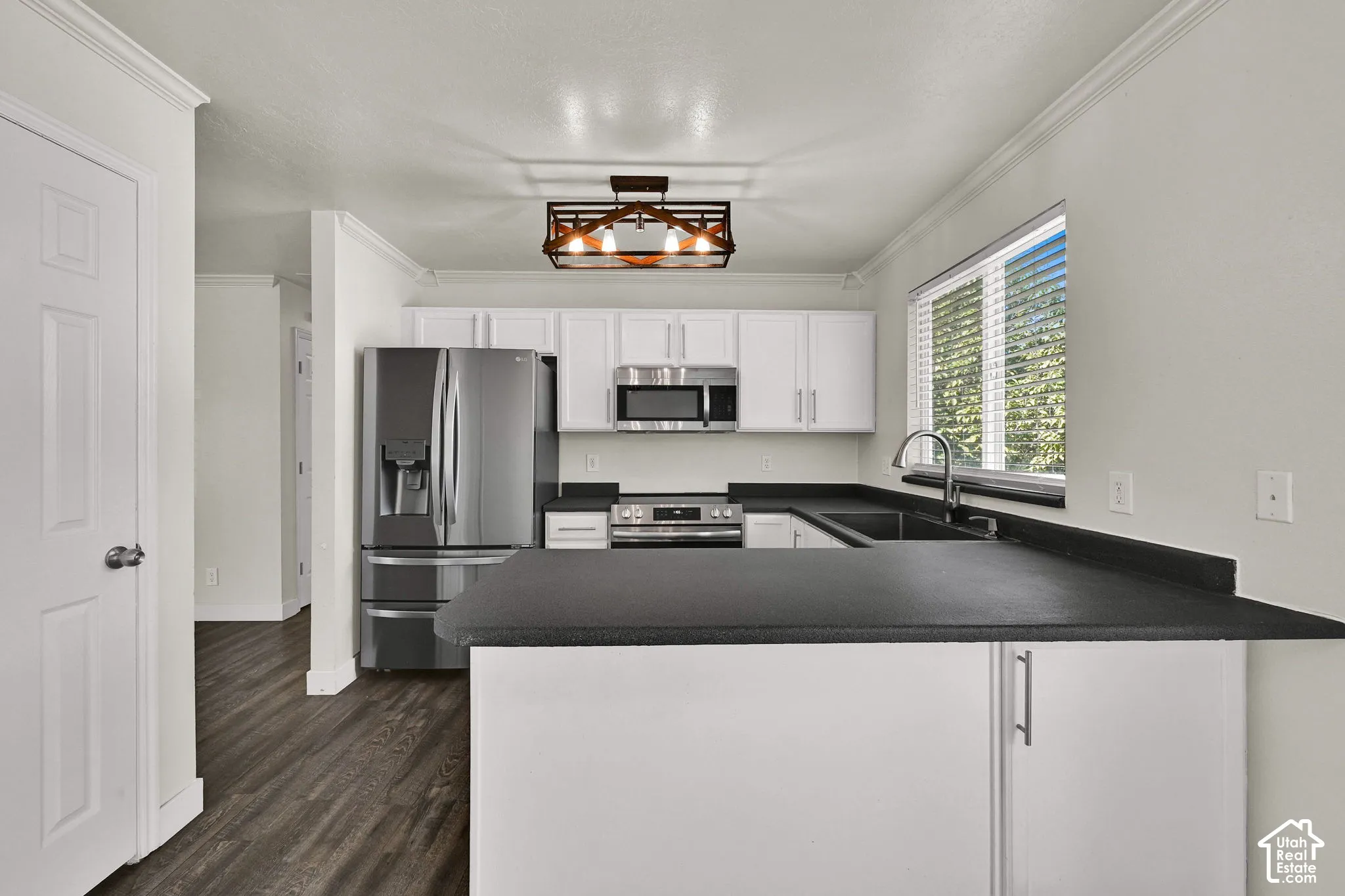 Kitchen featuring white cabinetry, dark countertops, stainless steel appliances, wood-finish flooring, and a decorative pendant light fixture