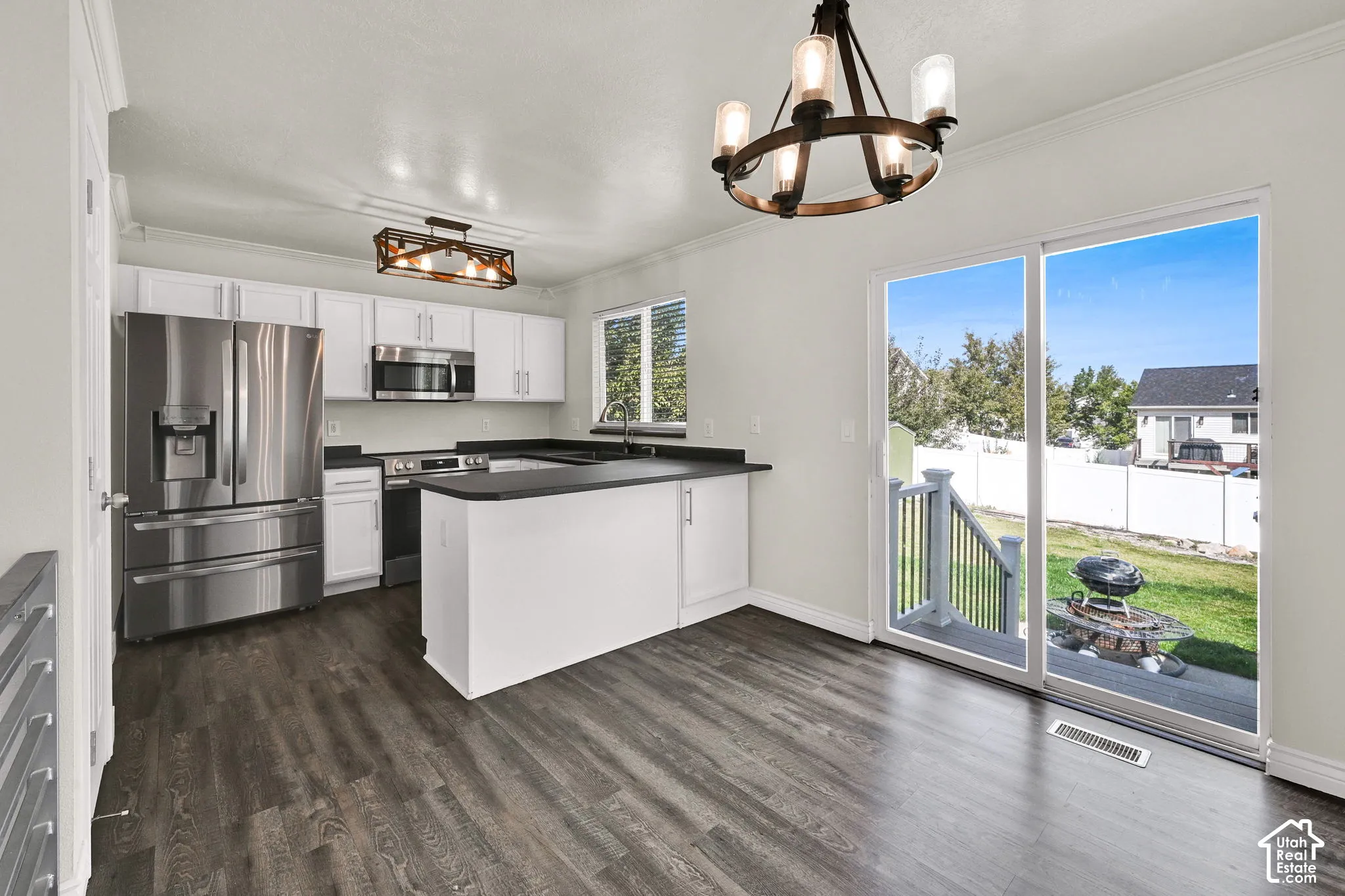 Kitchen featuring white shaker-style cabinetry, stainless steel appliances, dark contrasting countertops, wood-finish flooring, and dual rustic-style light fixtures