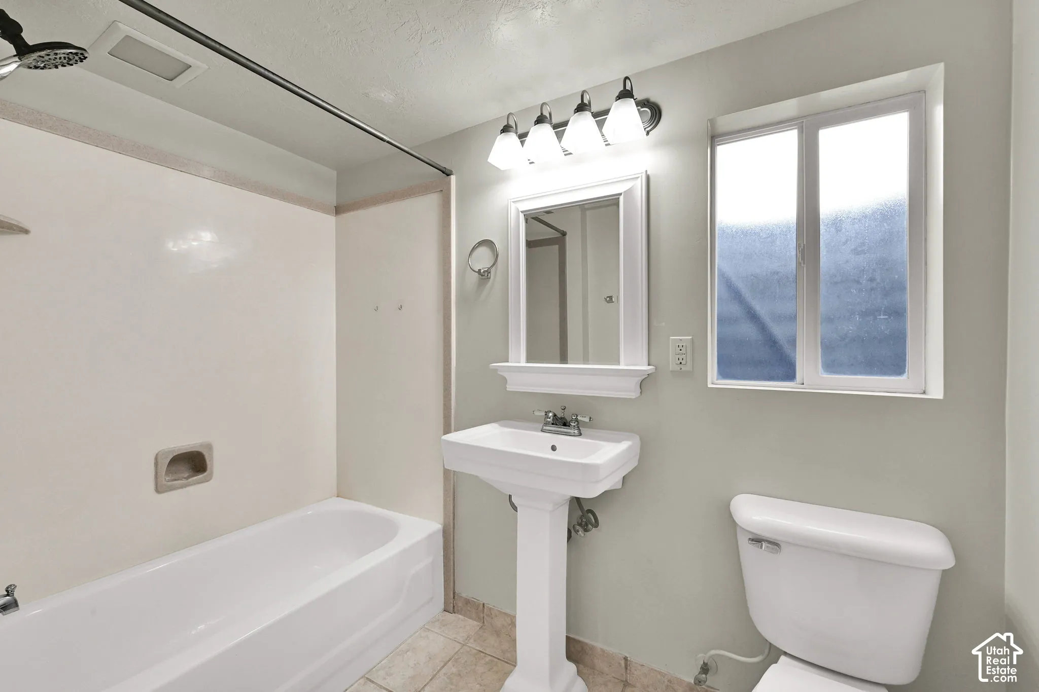 Bathroom featuring a white pedestal sink, framed wall mirror, four-light vanity fixture, bathtub with integrated surround, and window with frosted glass