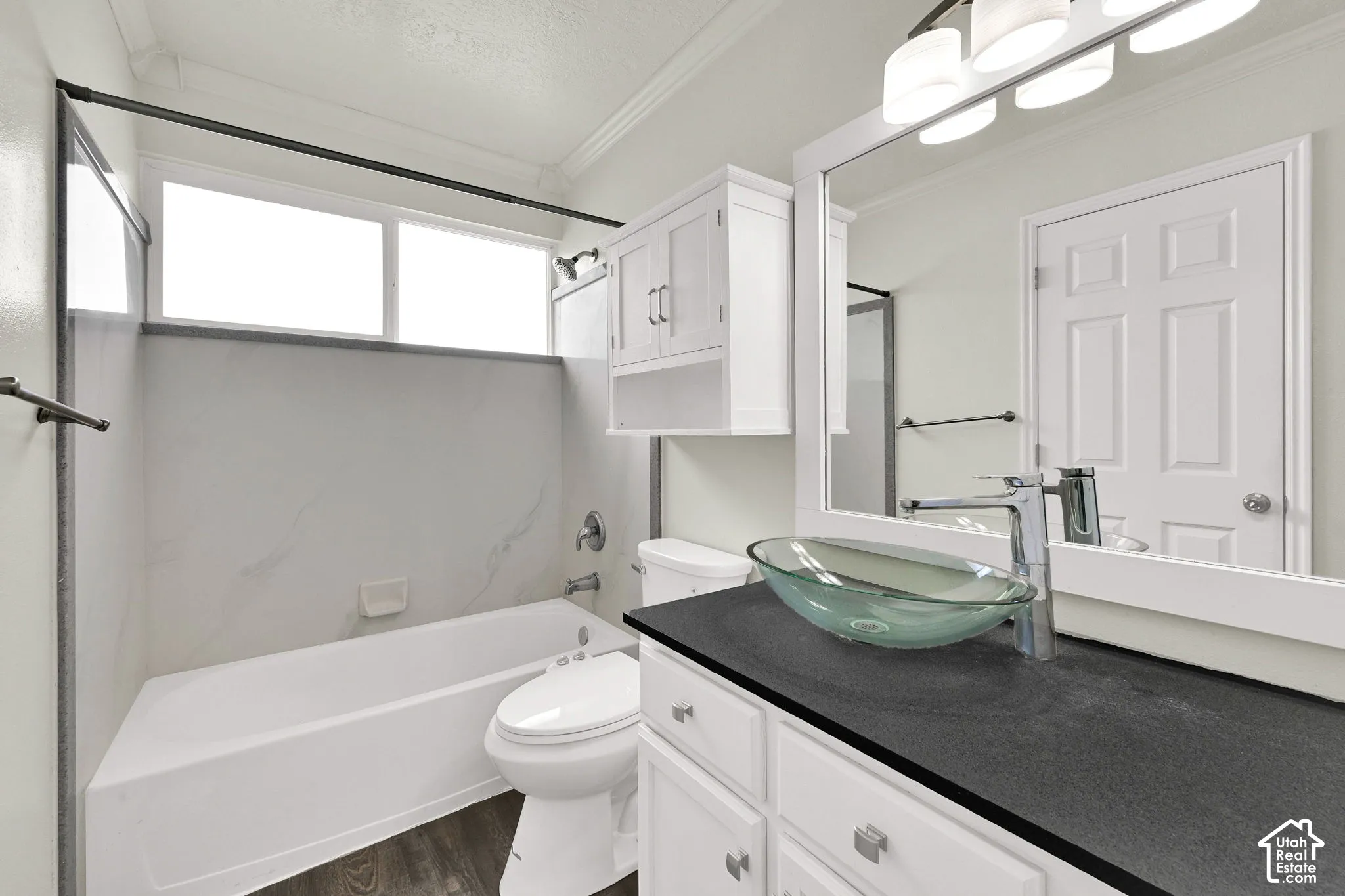 Bathroom featuring a vanity with dark stone-finish countertop, glass vessel sink, white shaker-style cabinetry, bathtub with surround, and overhead lighting