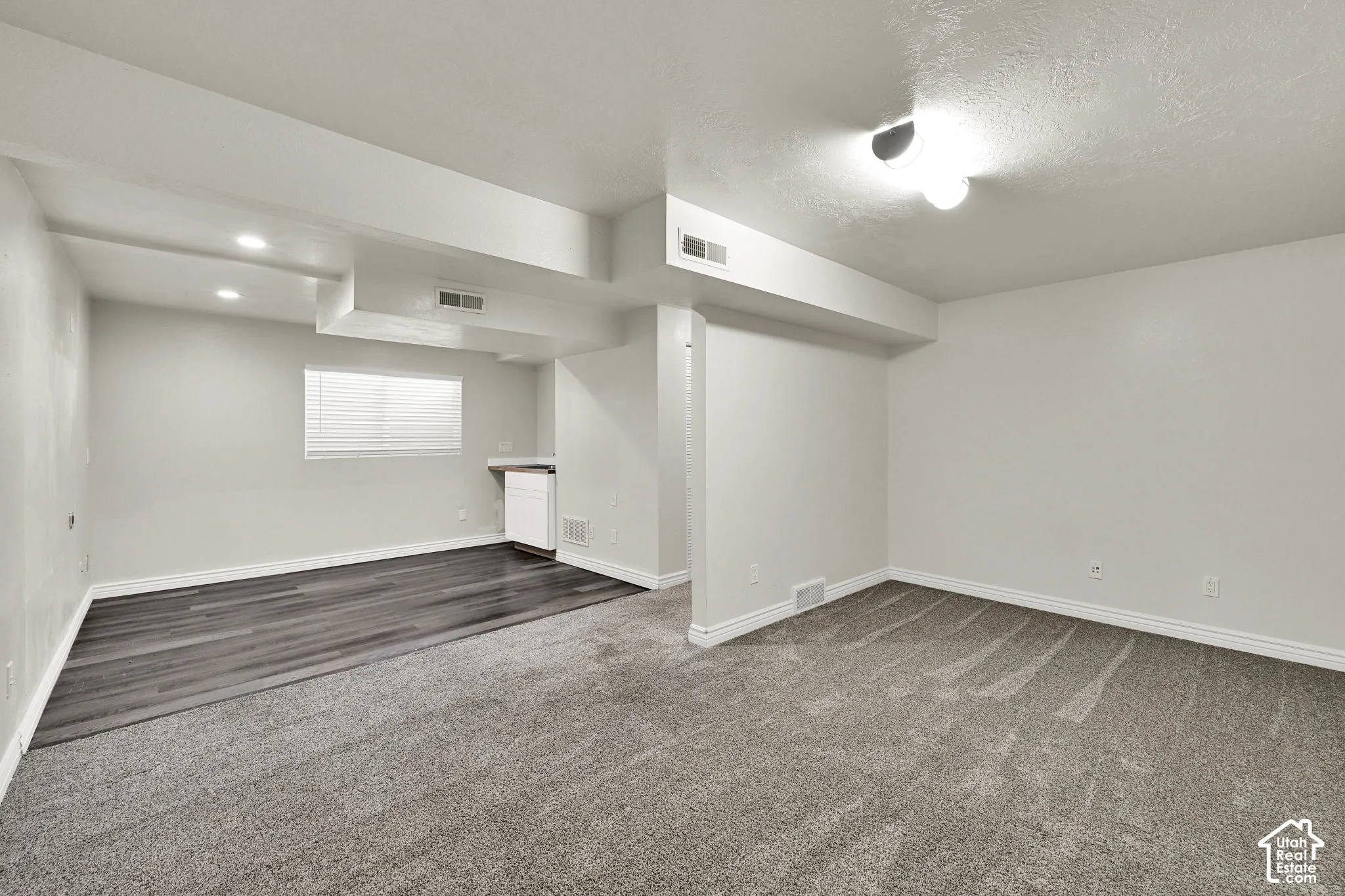 Interior space featuring neutral-toned walls, carpeting, wood-finish flooring, a white built-in cabinetry unit, and recessed lighting