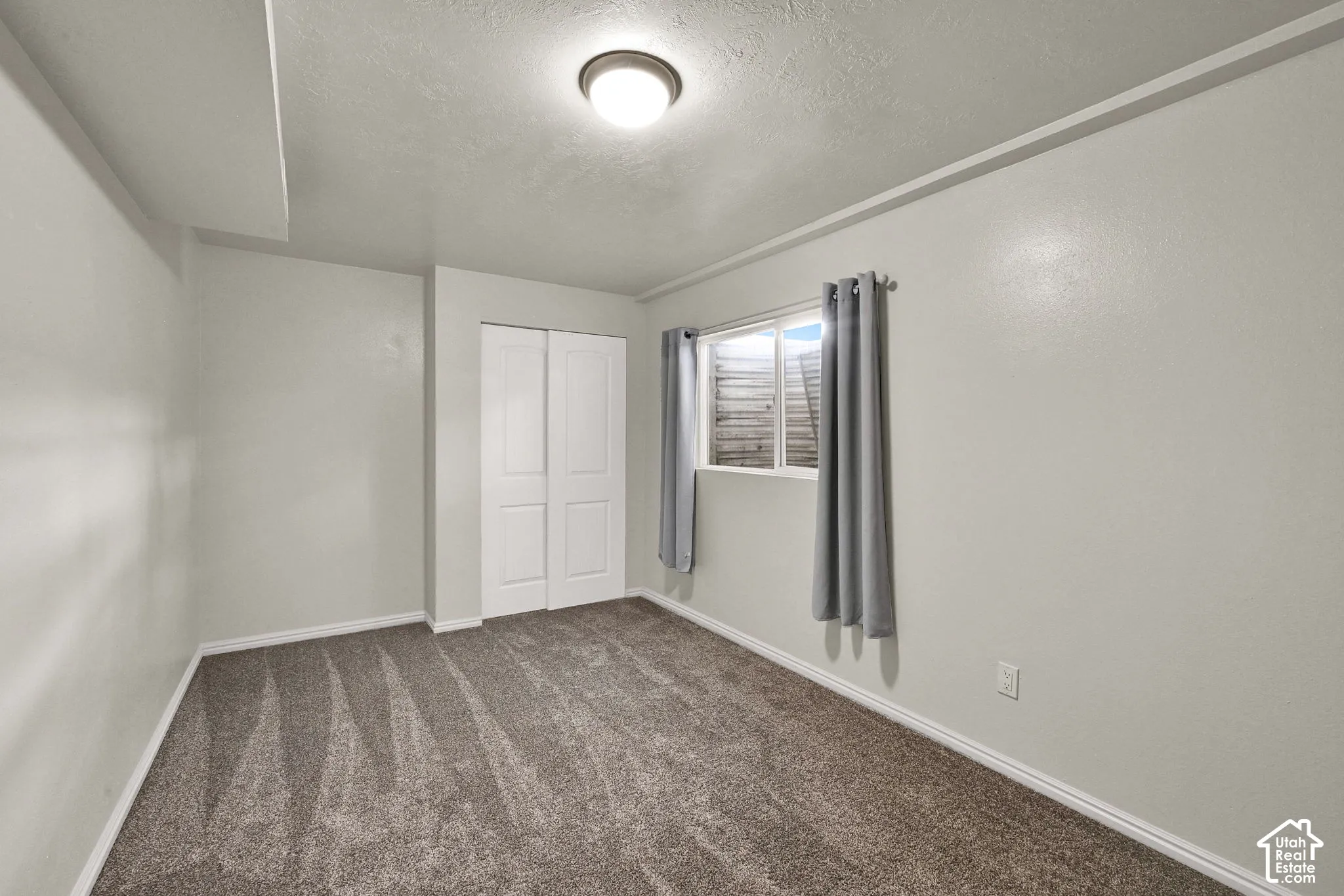 Neutral-toned room featuring wall-to-wall carpeting, a sliding-door closet, and a recessed window with an exterior well